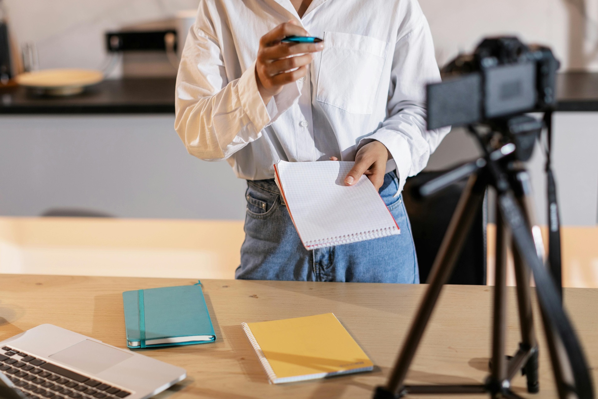 Photo of a woman from the neck down in front of a DSLR camera on a tripod, filming a presentation.