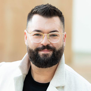 Headshot of a man with glasses, black beard, and white collared shirt.