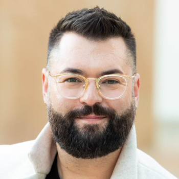 Headshot of a man with glasses, black beard, and white collared shirt.