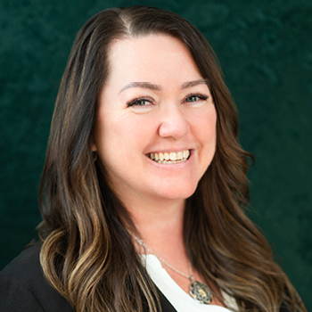 Headshot of a smiling woman with long brown hair and necklace.